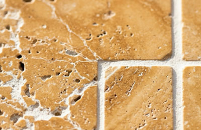 Macro gros plan sur un carreau de travertin bouché-poncé — trous naturels remplis, lumière rasante révélant la texture